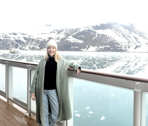 Advisor Becky Daniels standing on the deck of the Norwegian Encore cruise ship with Glacier Bay National Park in the background.